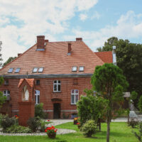 Współczesny widok Dworku na terenie Ośrodka Rehabilitacyjno-Wypoczynkowego w Sobieszewie, otoczonego zielenią.